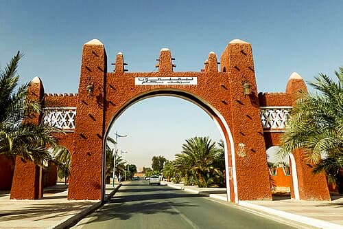 The red earthen entrance gate of Timimoun framed by palm trees